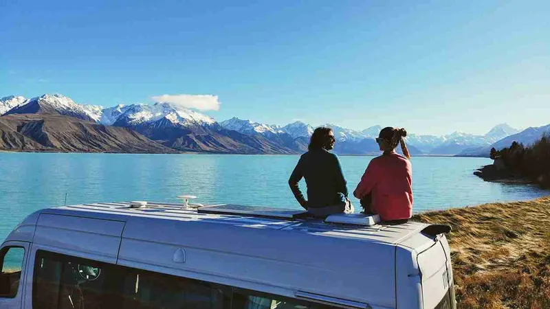 Dos personas sentadas en el techo de la campervan frente a un lago neozelandés