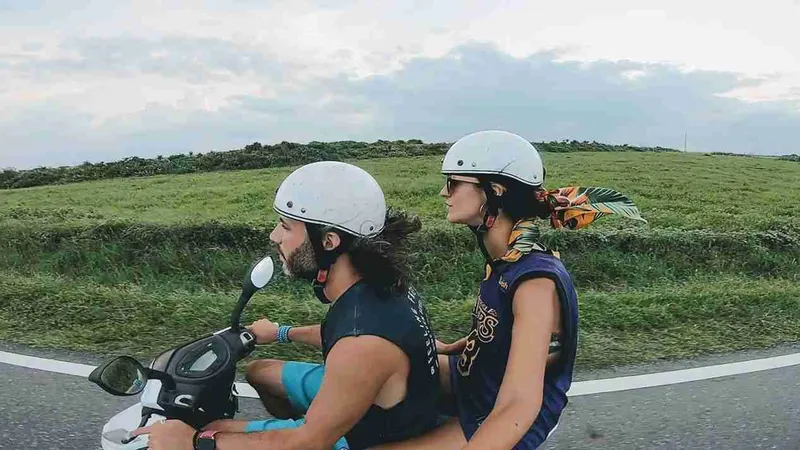 Pareja en moto con casco recorriendo Kenting entre campos verdes